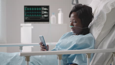 Black-woman-Patient-in-Hospital-with-Saline-Solution-Volumetric-Infusion-Pump-using-mobile-phone-on-examination-couch.-African-women-lying-in-hospital-bed-with-smart-mobile-phone-while-in-hospital.